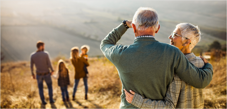 Elderly couple embracing with family in the background.